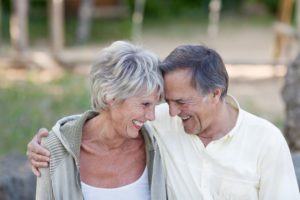 happy loving senior couple with head to head smiling in park